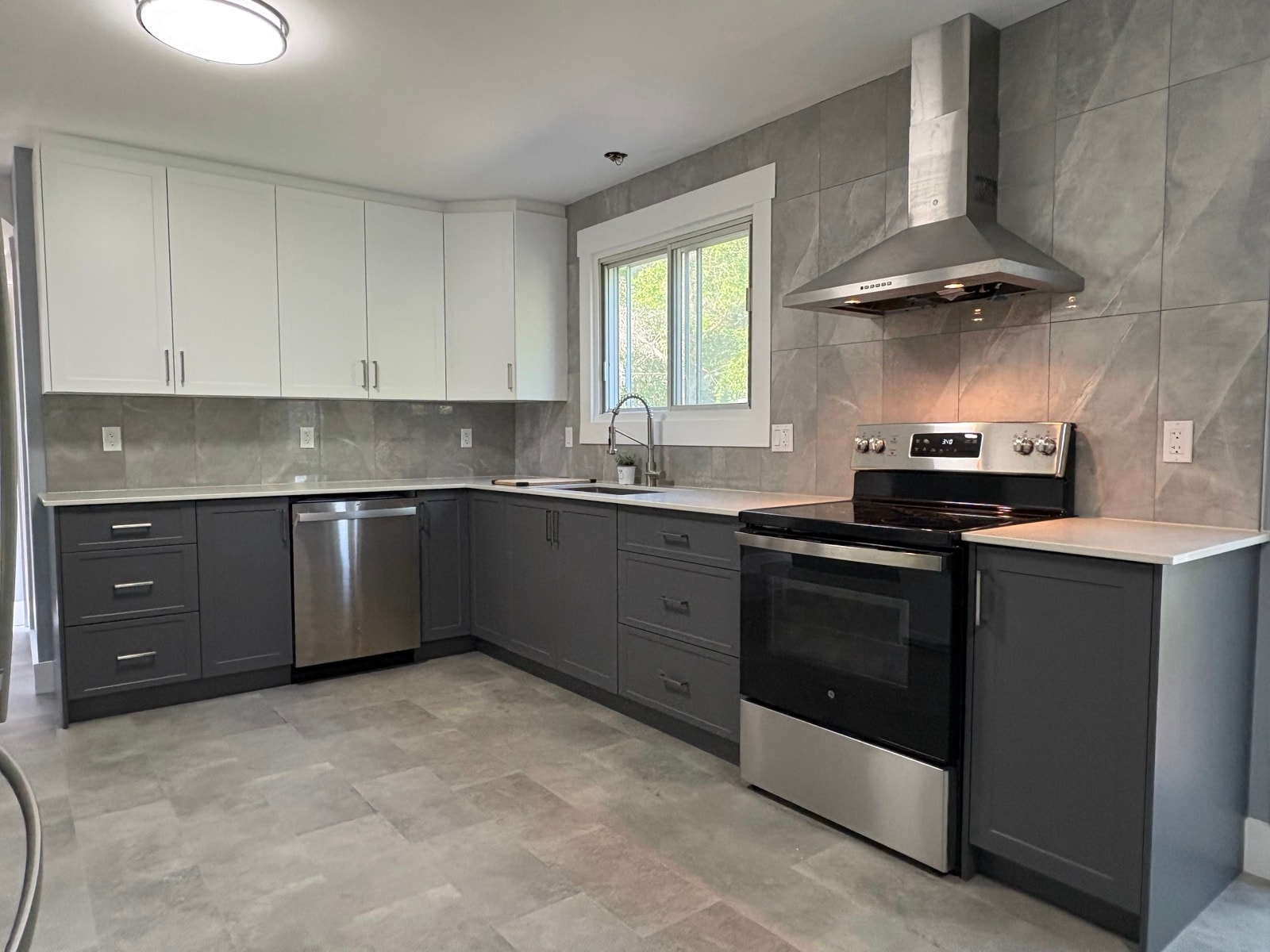 Grey and white two-tone shaker kitchen with large backsplash tiles, white quartz countertop and stainless steel appliances