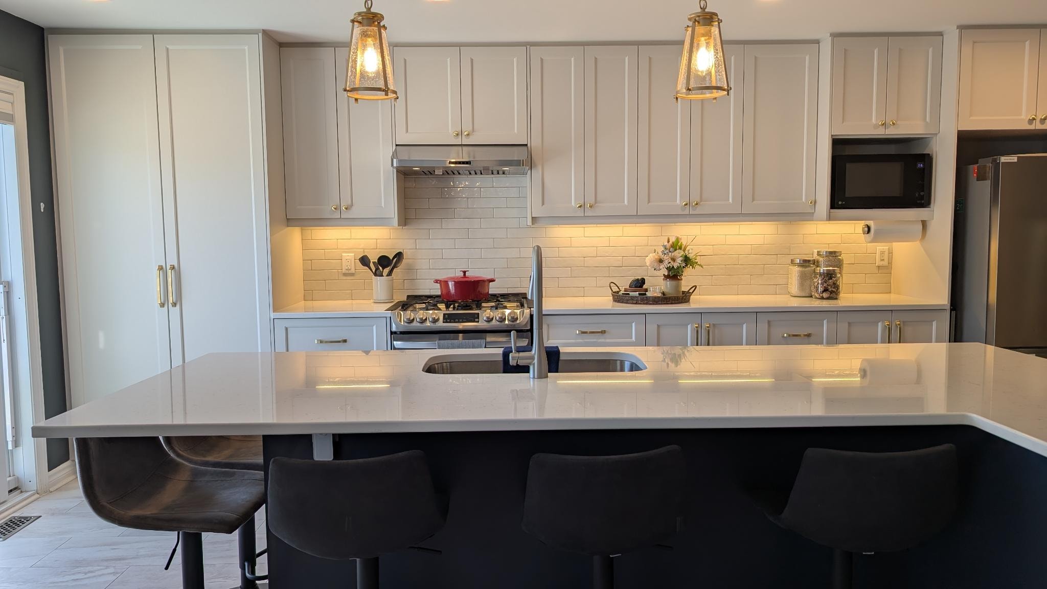White shaker kitchen with dark navy island, quartz countertop and gold pendant lights