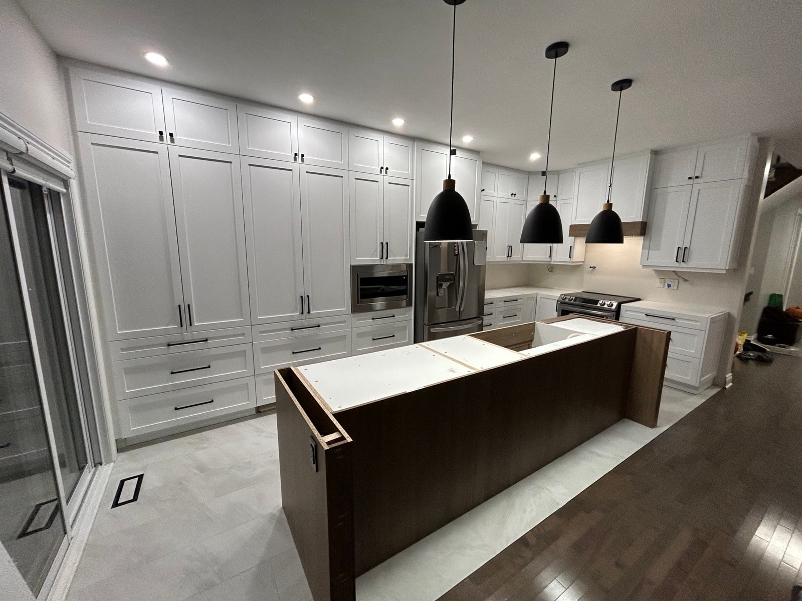 White shaker kitchen with large natural wood island, tall pantry cabinets, built-in microwave, stainless steel appliances and black hanging lights — Rockland, Ontario